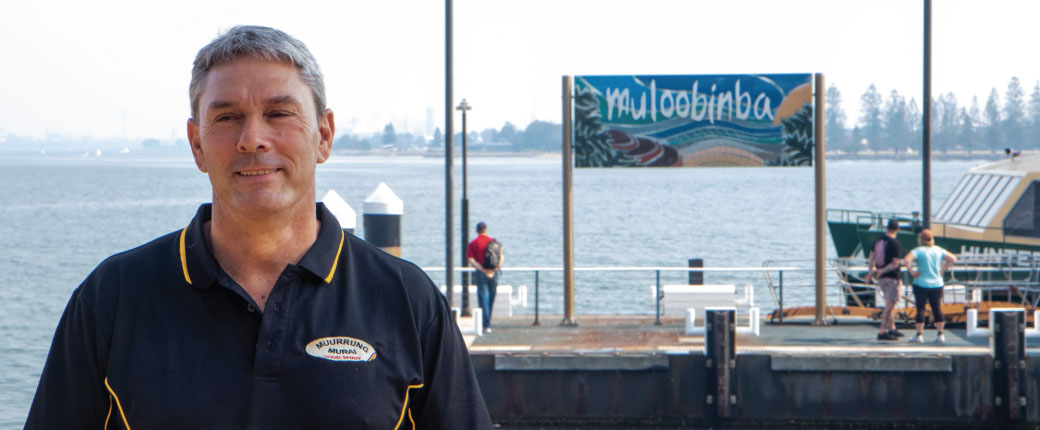 Amos standing in front of the Muloobina sign at Newcastle